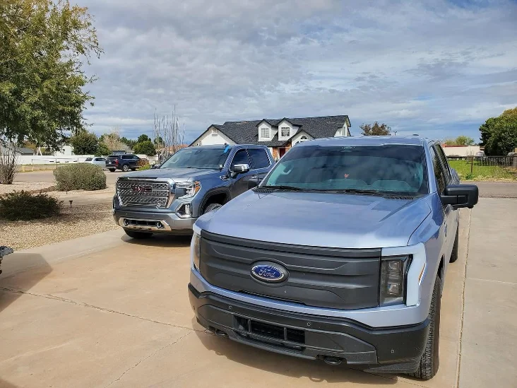 Image of a Ford truck and a GMC Sierra parked in a residential driveway with a cloudy sky in the background.